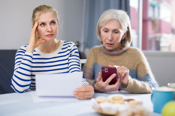 Focused mature woman and her adult daughter are studying an important document while sitting at a...
