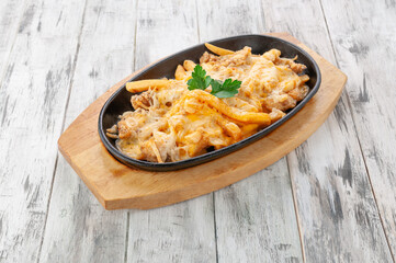 Poutine with chicken and french fries. Baked with cheese sauce. In a frying pan on a stand. Light wooden background. View from above.