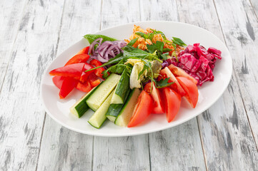 A set of snacks from chopped fresh vegetables and kim-chi cabbage. In a white plate. Light wooden background. View from above.