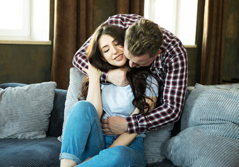 young couple in love hugging and kissing, sitting on sofa