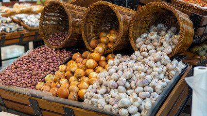 shallots, garlic and onions on display in a supermarket basket window. View from the side.