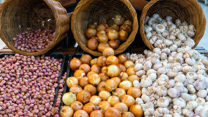 Shallots, garlic and onions on display in a supermarket basket window. View from the front.