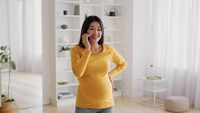 Phone Call. Beautiful pregnant asian woman talking on cellphone at home