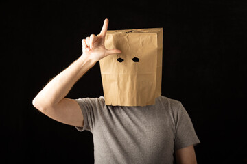 Man wearing a paper bag over his head and making a loser symbol