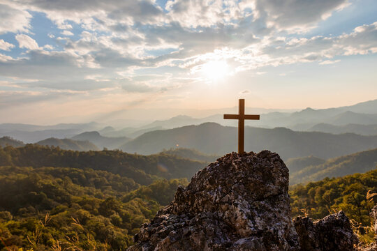 Crucifix symbol on top rock  mountain with bright sunbeam on the colorful sky background. Silhouettes