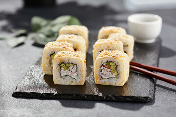 Maki sushi on dark stone table. Sushi roll crab, cheese, cucumber inside and tamago outside. Style concept japanese menu with black background, leaves and hard shadow.