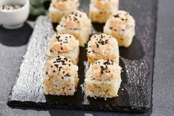 Maki sushi on dark stone table. Sushi roll in seasame and crab topped. Style concept japanesse menu with black background, leaves and hard shadow.