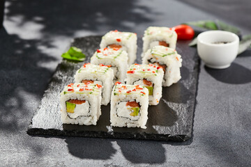 Fresh maki sushi on dark stone table. Colorful roll with vegetables. Sushi roll with salmon, avocado inside, cucumber outside. Style concept japanese menu with black background