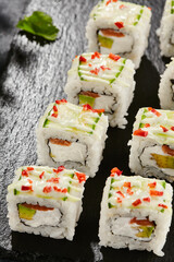 Fresh maki sushi on dark stone table. Colorful roll with vegetables. Sushi roll with salmon, avocado inside, cucumber outside. Style concept japanese menu with black background