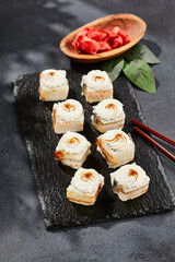 Maki sushi on dark slate. Unagi maki with eel. Sushi roll with eel fish, cream cheese and unagi sauce. Style concept japanese menu with black background, leaves and hard shadow.
