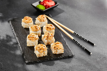 Baked Maki sushi on dark slate. Hot unagi maki with eel. Sushi roll with baked eel, cheese and unagi sauce topped. Style concept japanese menu with black background, leaves and hard shadow.