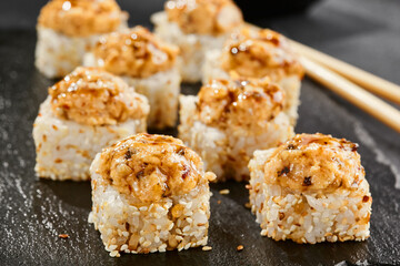 Baked Maki sushi on dark slate. Hot unagi maki with eel. Sushi roll with baked eel, cheese and unagi sauce topped. Style concept japanese menu with black background, leaves and hard shadow.
