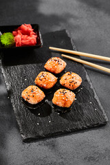 Baked Maki sushi on dark slate. Hot unagi maki with tobiko. Sushi roll with baked cheese, masago and unagi sauce topped. Style concept japanese menu with black background, leaves and hard shadow.