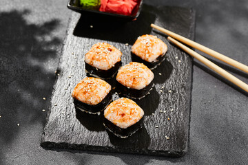 Baked Maki sushi on dark slate. Hot unagi maki with tobiko. Sushi roll with baked cheese, masago and unagi sauce topped. Style concept japanese menu with black background, leaves and hard shadow.