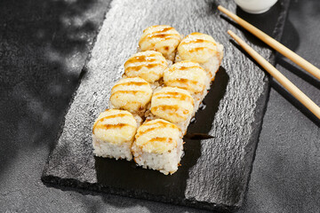 Baked Maki sushi on dark slate. Hot cheese maki with unagi sauce. Sushi roll with baked cheese and unagi sauce topped. Style concept japanese menu with black background, leaves and hard shadow.