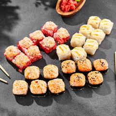 Hot maki set on dark slate. Baked sushi set with variety rolls. Sushi rolls with salmon,tobiko, crab and baked cheese topped. Style concept sushi menu with black background, leaves and hard shadow.