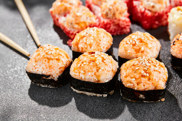 Hot maki set on dark slate. Baked sushi set with variety rolls. Sushi rolls with salmon,tobiko, crab and baked cheese topped. Style concept sushi menu with black background, leaves and hard shadow.