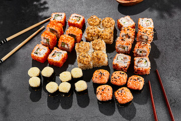 Maki sushi set on dark background. Maki set with variety rolls. Composition from sushi rolls and baked maki . Style concept sushi menu with black background, leaves and hard shadow.