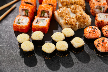 Maki sushi set on dark background. Maki set with variety rolls. Composition from sushi rolls and baked maki . Style concept sushi menu with black background, leaves and hard shadow.