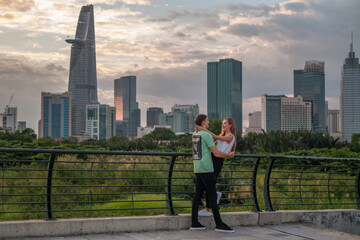 Lovely mixed couple standing on the bridge in the park in metropolis and cuddling. Love people and happiness concept. Skyscrapers on the background
