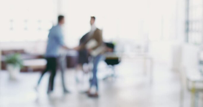 Concepts of modern business. Defocused businesspeople at work in a modern office. Two blurred businessmen shaking hands in greeting. Group of coworkers meeting, shaking hands.