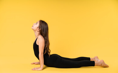 girl gymnast studio. little gymnast trains, shows a gymnastic element. do sport. Isolated on a colored yellow background. Young girl gymnast