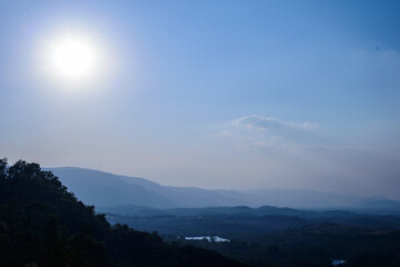 The sun with blue sky over silhouette mountain.
