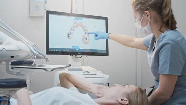 Girl doctor dentist demonstrates a 3D model of teeth on a touch monitor, rotates her hands. Dental consultation in the clinic, diagnostics. Jaw scan, digital imprint, medical digital technology.