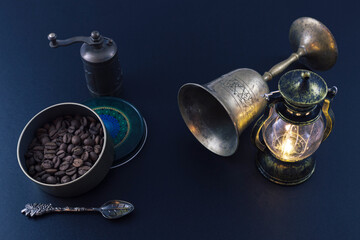 Coffee beans in a round box, a burning lantern and an ancient bronze cup on a black background