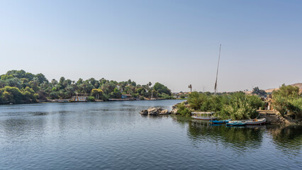 Fototapeta na wymiar On the banks of the Nile, lush green vegetation, picturesque boulders. The boats are on calm water. Clear blue sky. Reflection. Egypt