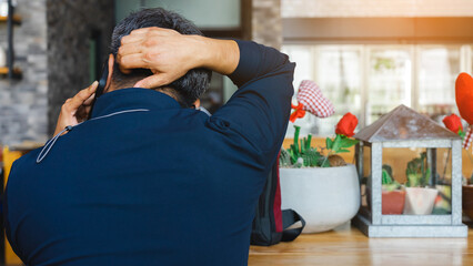 Back view of busy mature businessman calling his wife in cafe on Valentines day with red heart ornaments and rose blurred in background.Selective focus on mobile phone.Love and Valentines day concept