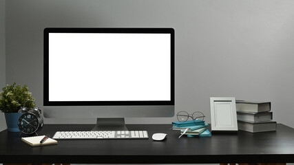 Mockup computer pc with white display, alarm clock, houseplant and picture frame on black table.