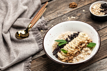 Oatmeal with dried raisins, banana and walnuts decorated with mint, Healthy diet vegetarian breakfast or snack, Clean eating, dieting, vegan food concept. top view