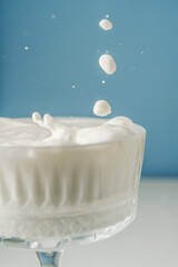 Milk pours into a beautiful crystal glass on a blue background and splashes around.