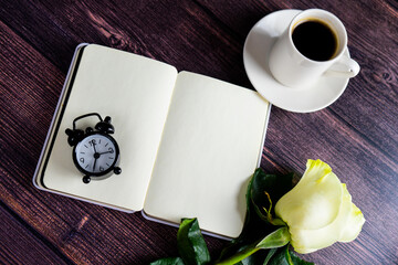 A notebook, a beautiful rose flower and an alarm clock with a coffee cup, on the background of a...