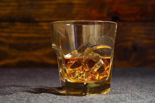 A glass of whiskey labeled Jameson with ice cubes stands against a background of dark oak boards. Close-up.