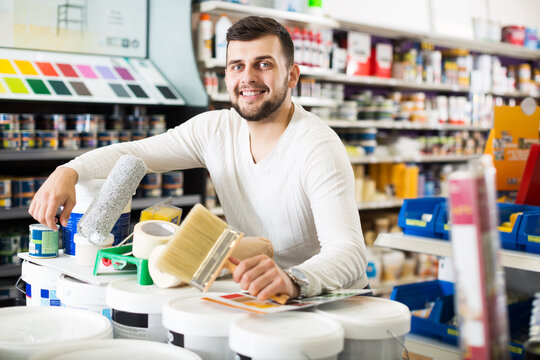 Smiling young man buying tools for house decoration in paint supplies store