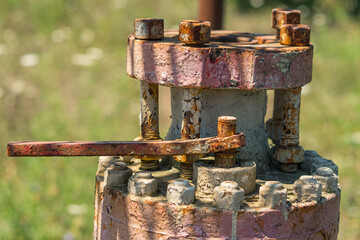 An old flange with rusty bolts and peeling paint abandoned in the field after the end of oil production. Pollution of the environment.