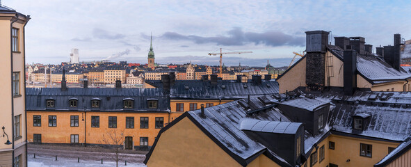 View over old 1700s yellow houses with dorms and chimneys on black tin roofs from a view point in the district Södermalm and the skyline of the old town Gamla Stan a cold sunny winter day in Stockholm