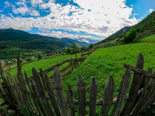 Fototapeta na wymiar A fence and an amazing view on the valley in Mestia in the Greater Caucasus Mountain Range, Upper Svaneti, Country of Georgia. Clouds cover the snow capped mountain peaks.Freedom,Outdoor,Trekking