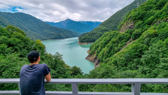 A man with a panoramic view on the Jvari reservoir on river Enguri (Inguri). Beautiful mountain landscape. Lake with turquoise colored water surrounded by Caucasus mountains,Svaneti Region in Georgia.