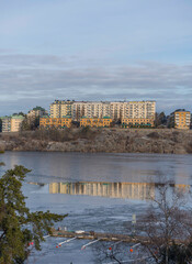 Apartment houses at the waterfront of the district island Kungsholmen skyline with functionalist houses on a cliff and ice floats and reflections a cold sunny winter day in Stockholm - obrazy, fototapety, plakaty