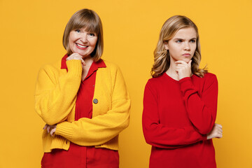 Happy caucasian woman 50s in red shirt with teenager girl 12-13 years old. Grandmother frowning sad granddaughter prop up chin look aside isolated on plain yellow background. Family lifestyle concept.