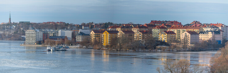 Fototapeta na wymiar Panorama view over the island Lilla Essingen at an icy bay of the lake Mälaren with apartment houses, jetties and bridges a cold sunny winter day in Stockholm