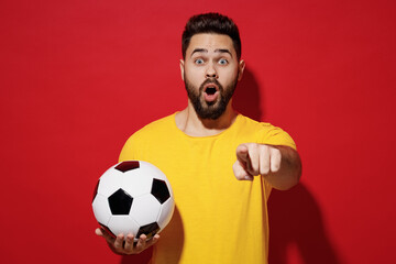 Surprised young bearded man football fan in yellow t-shirt cheer up support favorite team hold...