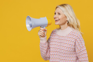 Side view elderly smiling blonde woman 50s in pink sweater hold scream in megaphone announce...