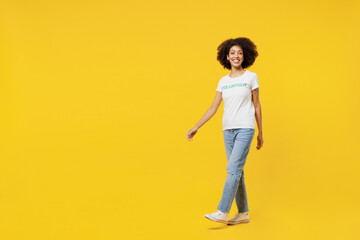 Fototapeta premium Full body fun young smiling woman of African American ethnicity wears white volunteer t-shirt walk going stroll isolated on plain yellow background. Voluntary free work assistance help grace concept.