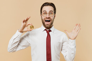 Young overjoyed employee business man corporate lawyer 20s in classic white shirt red tie glasses work in office holding bitcoin coin currency spread hand isolated on plain beige background studio