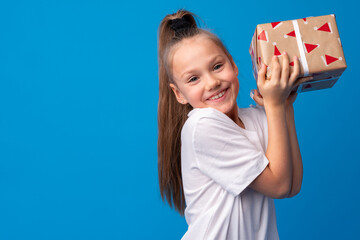 Happy little girl with long hair holding a gift box on a blue background