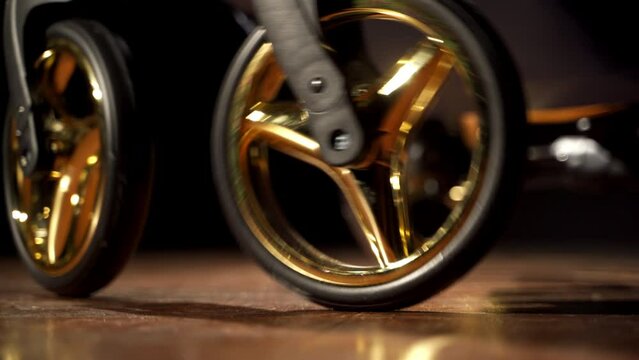 Shiny wheels being turned and spark in the light. Black baby pram pushed in dark room. Close up.